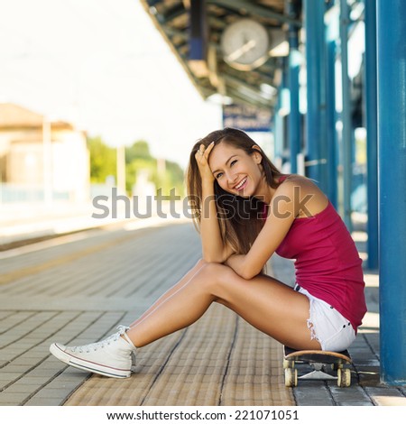 Happy teenager with skateboard portrait in train station.