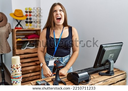 Young brunette woman holding banner with open text at retail shop angry and mad screaming frustrated and furious, shouting with anger. rage and aggressive concept. 