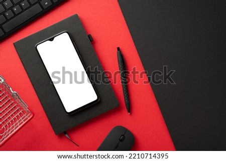Black friday concept. Top view photo of smartphone keyboard computer mouse planner pen and shopping cart on bicolor red and black background with empty space