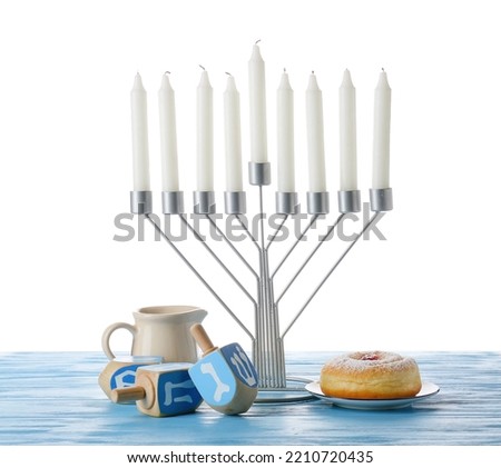 Menorah with candles, dreidels and donut for Hanukkah celebration on color wooden table against white background