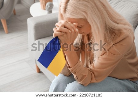 Mature woman with flag of Ukraine praying at home, closeup