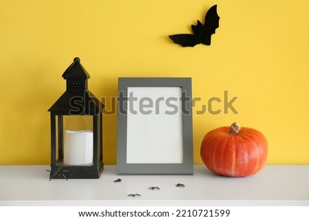 Blank photo frame with Halloween pumpkin, lantern and spiders on mantelpiece near yellow wall