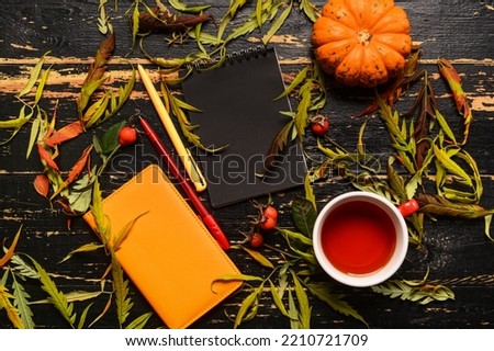 Notebooks, cup of tea, pumpkin and autumn decor on dark wooden background