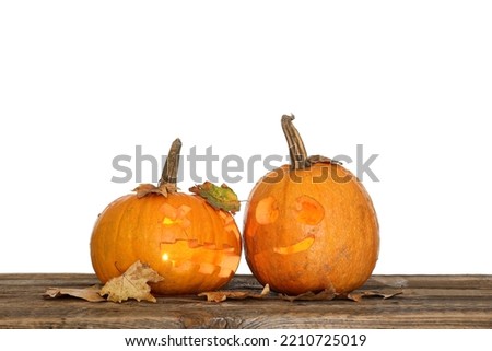 Carved Halloween pumpkins with fallen leaves on table against white background