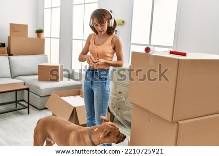 Young caucasian woman listening to music feeding dog at home