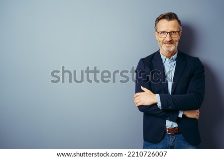 Self-assured attractive middle-aged man standing with folded arms smiling at the camera over a blue studio background with copy space