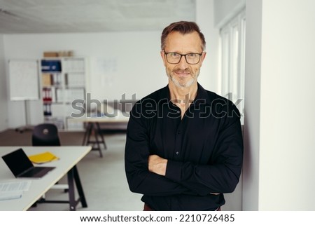 Portrait of smiling senior man standing in office corridor wearing glasses