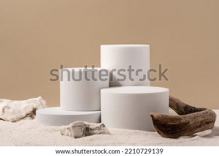 Natural cosmetic background for product presentation. Driftwood, stones and white podium on the sand. Front view.