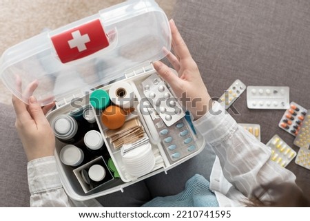 Closeup female hand neatly placing medicament at domestic first aid kit top view. Storage organization in transparent plastic box drug, pill, syringe, bandage. Fast health help safety emergency supply Royalty-Free Stock Photo #2210741595