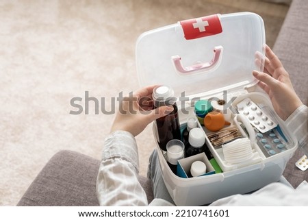 Closeup female hand neatly placing medicament at domestic first aid kit top view. Storage organization in transparent plastic box drug, pill, syringe, bandage. Fast health help safety emergency supply Royalty-Free Stock Photo #2210741601