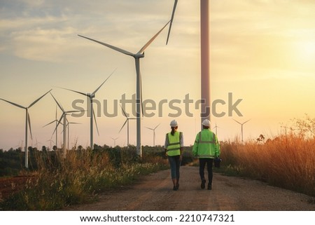 Back view of young maintenance engineers team working in wind turbine farm at sunset. Royalty-Free Stock Photo #2210747321