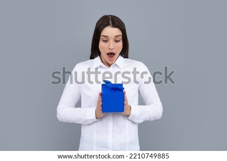 Portrait of a funny surprised girl with gift box isolated over gray background. Woman holding gift present.