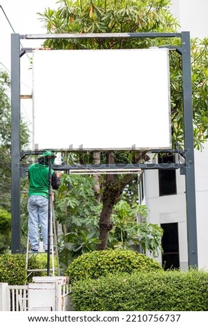 An Asian worker is using a brush to paint a sign outside a building.