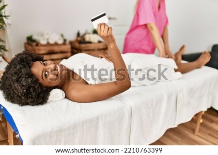 Young african american woman holding credit card having legs massage at beauty center