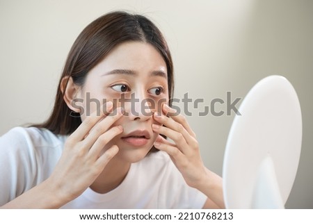Sleepless Asian woman looking her face in the mirror and worry about dark circles under eyes