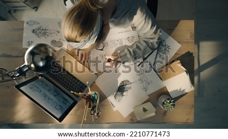 Young woman working on a storyboard in a design studio. A laptop and stationary jar on the table. Woman drawing sketches as a roadmap for the video.