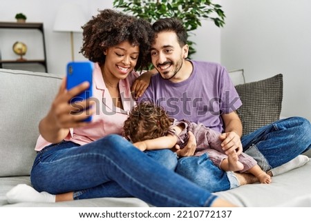Couple and daughter make selfie by the smartphone sitting on sofa at home