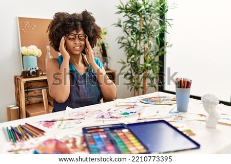 Beautiful african american woman with afro hair painting at art studio with hand on head for pain in head because stress. suffering migraine. 