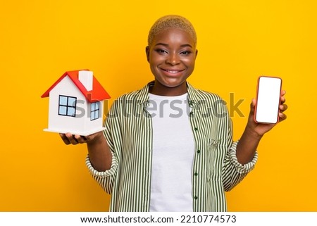 Photo of nice cheerful person arms hold little house show empty space telephone screen isolated on yellow color background