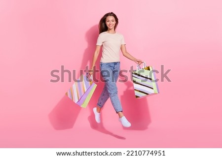 Full size photo of excited active girl hold packages jumping isolated on pink color background