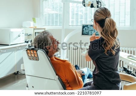 An Anonymous Female Dentist Explaining Teeth X-ray on a Digital Tablet to Smiling Mature Patient at Dentist's Office Royalty-Free Stock Photo #2210781097