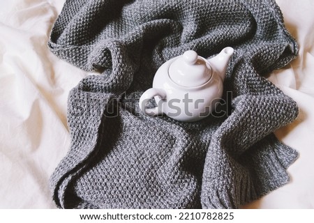 Home feel cozy in winter. Gray woolen scarf and porcelain teapot flat lay photo. Warm atmosphere in home