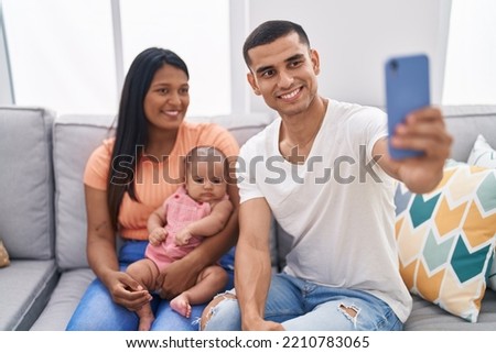 Hispanic family using smartphone sitting on sofa at home