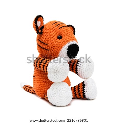 Plush tiger in orange, white and black, made using the amigurumi crochet technique seen from the side, sitting on a white background.