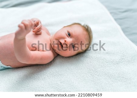 White newborn baby in a diaper lying on blanket on floor looking into camera with curious expression. Changing a baby. Horizontal indoor shot. High quality photo