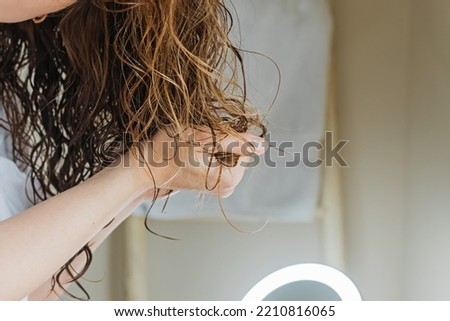 Woman scrunching her hair to form curls. Applying curly method for hair styling. Close-up on the hands Royalty-Free Stock Photo #2210816065