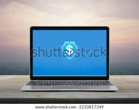 Dollar with shield flat icon on modern laptop computer monitor screen on wooden table over office city tower and skyscraper at sunset sky, vintage style, Business money insurance and protection online