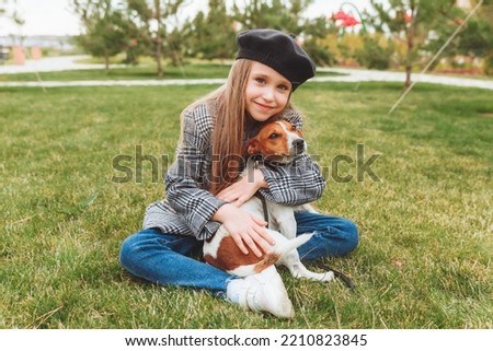 a little girl kisses and hugs her Jack Russell terrier dog in the park. Love between the owner and the dog. a child is holding a dog in his arms.