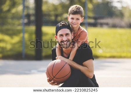 A man and young boy playing basketball on a court, teaching little player and spending time outdoors