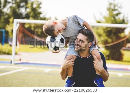 A man with child playing football outside on field