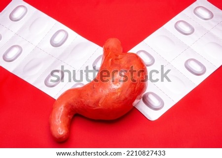 The anatomical figure of the human stomach on a red background, along with two blisters of pills for stomach pain. Photo for use in gastroenterology or internal medicine. Royalty-Free Stock Photo #2210827433