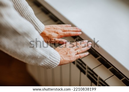 Woman's hands in winter sweater is touching home radiator and feeling cold. Social media concept. Focus is at hands Royalty-Free Stock Photo #2210838199