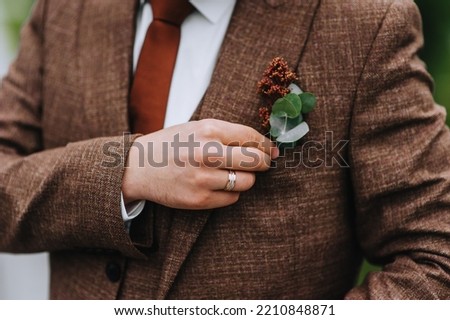 Close-up portrait of the groom in a brown, expensive, stylish suit with a boutonniere, tie and a gold ring on his finger. wedding photography.