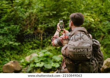 Happy white man taking photo on cellphone while hiking in forest