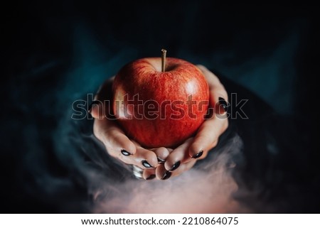 Woman as witch offers red apple - symbol of toxic proposal, lure. Fairytale, white snow, wizard concept. Halloween celebration, cosplay. Smoke, mist background. Royalty-Free Stock Photo #2210864075