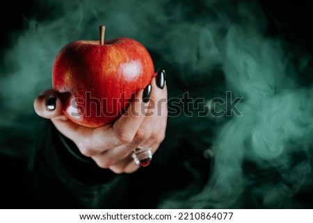 Woman as witch offers red apple as symbol of temptation, poison. Fairy tale, white snow wizard concept. Spooky halloween, cosplay. Smoke, haze background. Royalty-Free Stock Photo #2210864077