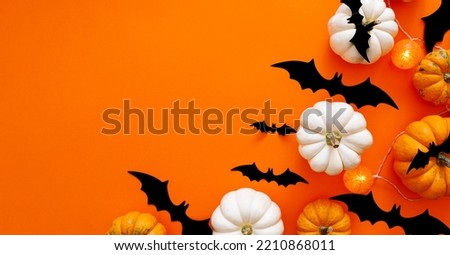 Halloween flat lay composition of black paper bats And pumpkins on orange background. Halloween concept.