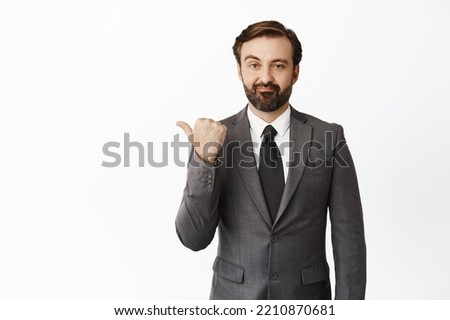Skeptical male entrepreneur pointing left, looking with disappointed, upset face expression, standing in grey suit over white background