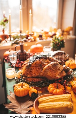 Classic USA Thanksgiving day dinner with holiday autumn decor and candles. Family dining room table set with delicious golden roasted turkey on platter garnished rosemary and fresh small pumpkins