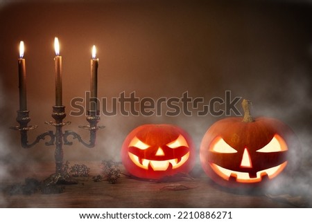 Halloween pumpkin head, Jack O Lantern, on wooden background. Spooky halloween pumpkins, Jack O Lantern, with an evil face and eyes and old candles with a mist on dark background.