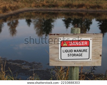 A warning sign posted at the edge of a large livestock manure storage lagoon