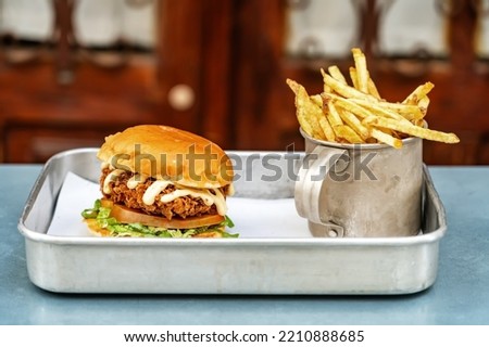 Classic hamburger with meat salad mayonnaise and fried potatoes in an aluminum mug on a tray. Close-up.