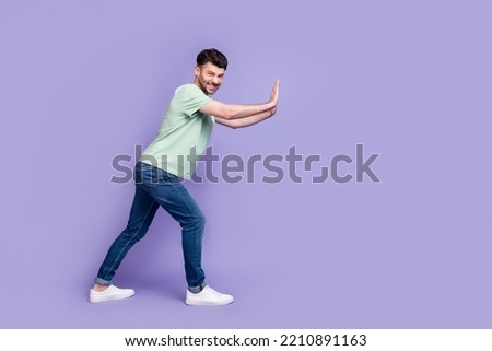 Full body photo of attractive young guy pushing hard copyspace difficult wear trendy gray clothes isolated on violet color background Royalty-Free Stock Photo #2210891163