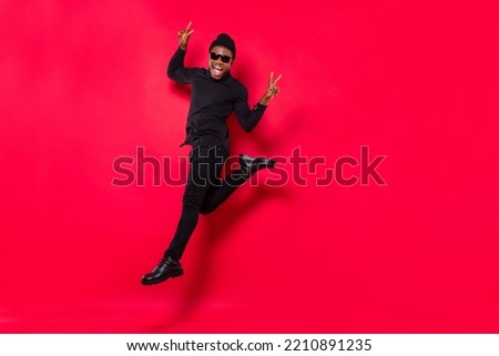 Full length body size view of handsome trendy cheerful guy jumping showing v-sign isolated over bright red color background