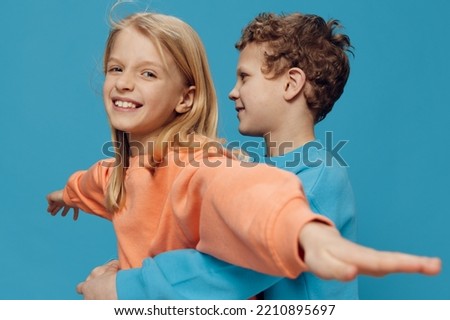 cute, beautiful, happy children, brother and sister stand in bright clothes on a blue background and the boy hugs the girl from the back. Studio photography with blank space for advertising mockup