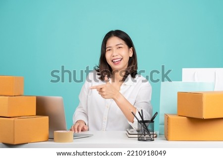 Young Asian woman in casual shirt sit work at desk with a brown cardboard box and point index finger on pc laptop. She using internet online isolated on green background.